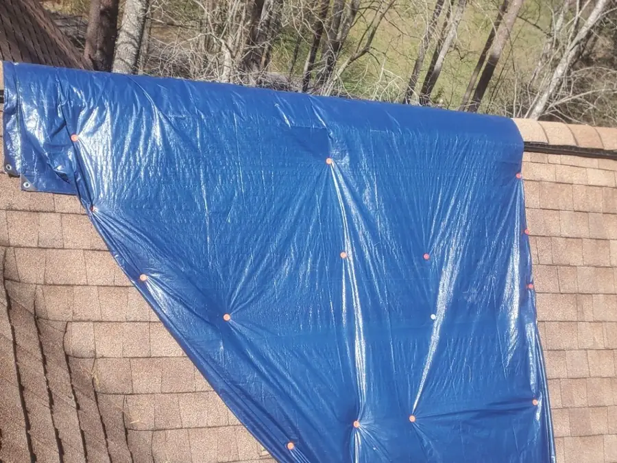 Emergency tarp secured over a storm-opened section of shingle roof