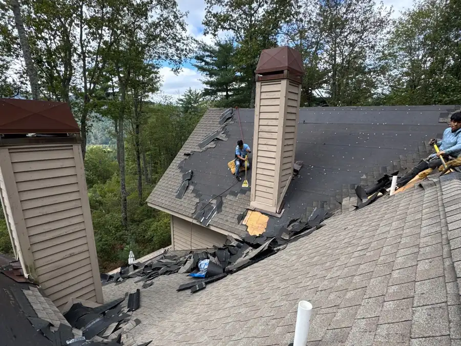 Crew stripping shingles around a chimney during a full roof replacement